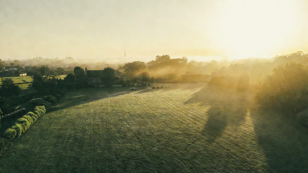 Aerial view of a green rural property at sunrise with morning mist