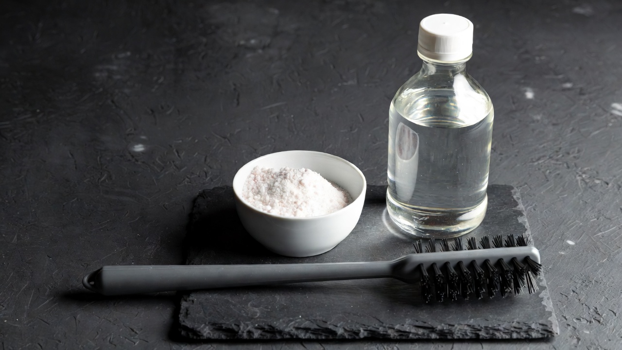 Baking soda, white vinegar bottle, and drain brush on dark slate surface